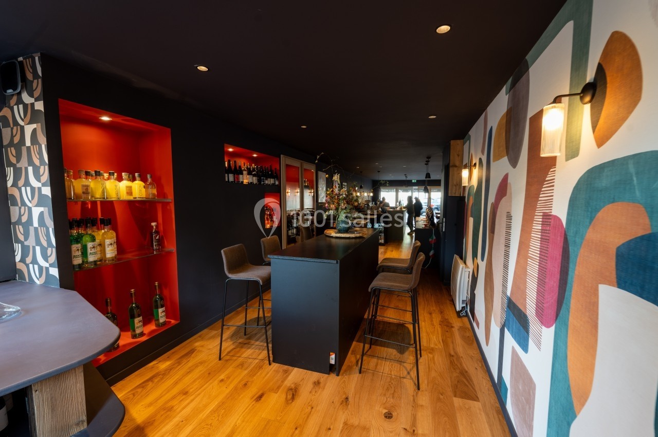 Intérieur d'un bar moderne avec comptoir central, étagères éclairées rouges et décoration murale colorée.