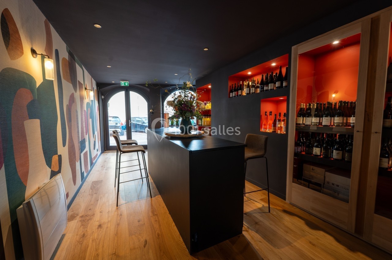 Intérieur d'un bar à vin moderne avec un comptoir central, des étagères de bouteilles et une décoration murale colorée.