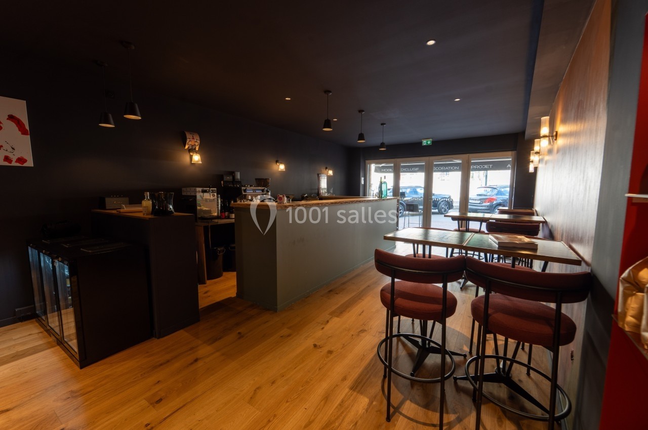 Intérieur d'un café moderne avec comptoir en bois, tables hautes et éclairage tamisé.