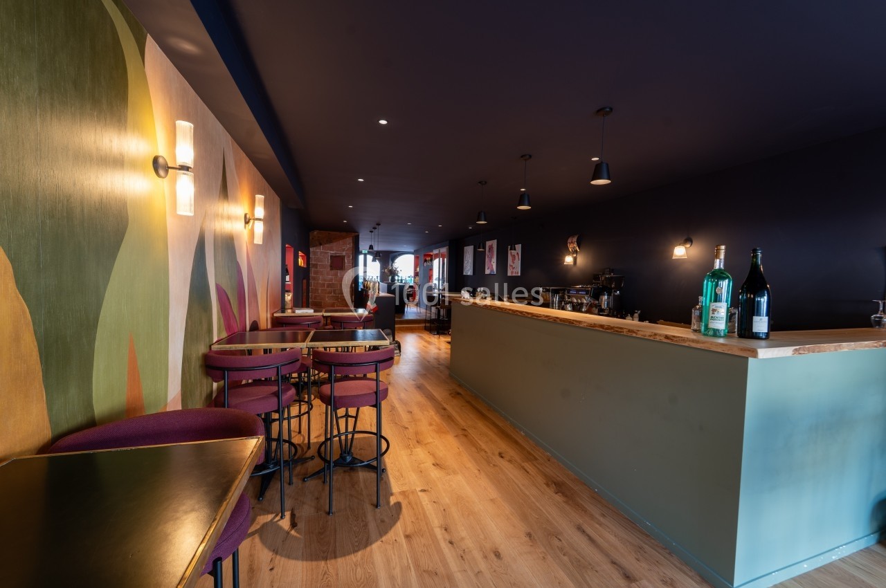 Intérieur d'un café moderne avec un comptoir en bois, des tables hautes et une décoration murale colorée.