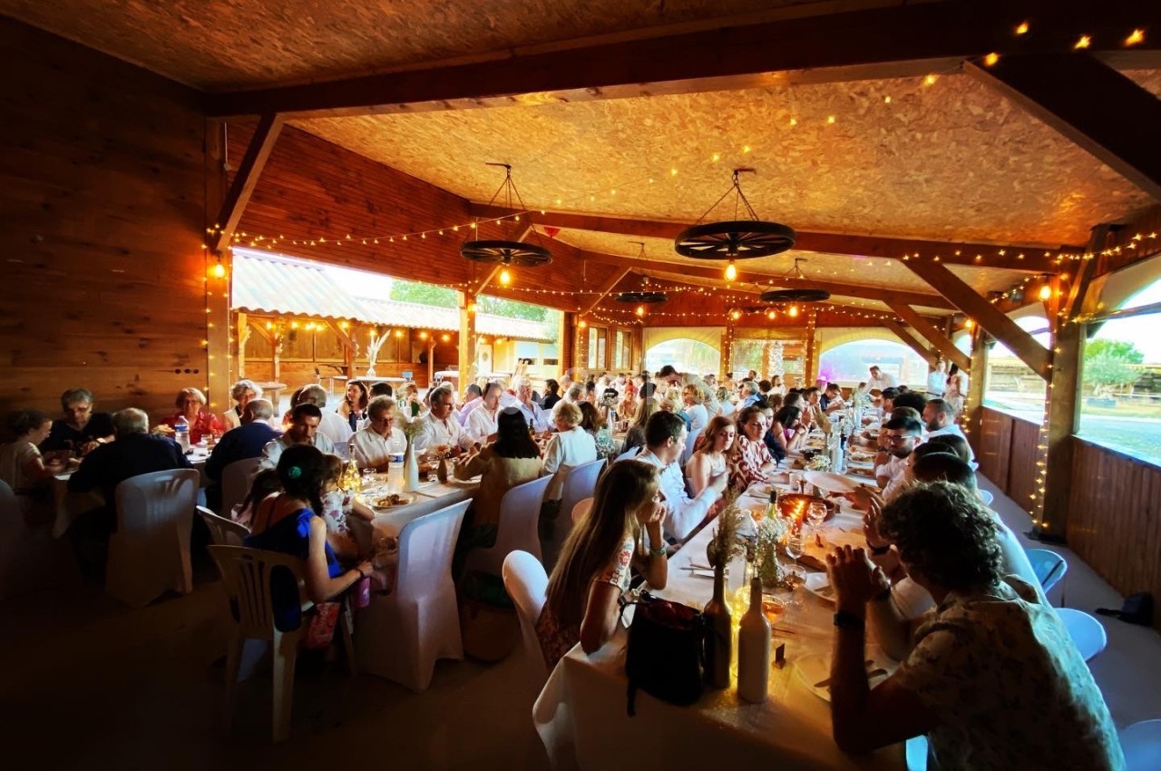 Des convives assis à de longues tables décorées, partageant un repas dans une grande salle en bois éclairée par des…