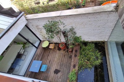 Façade d'une maison moderne en bois avec de grandes baies vitrées, entourée de murs en briques et végétation.