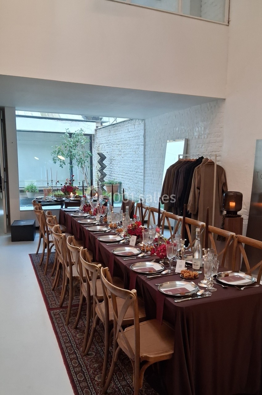 Table dressée avec nappes bordeaux, vaisselle élégante et décorations florales dans une salle lumineuse au style épuré.