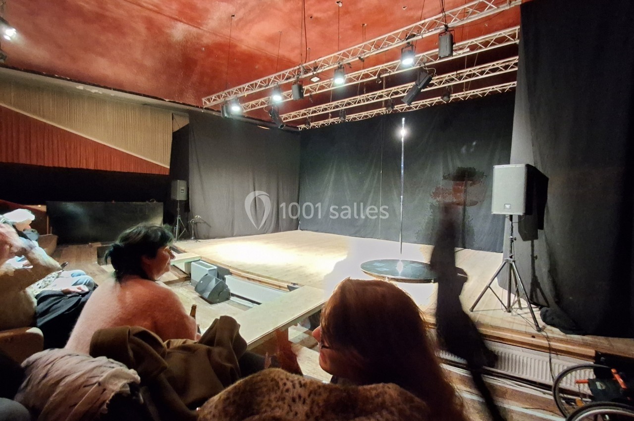 Une petite scène éclairée dans une salle de spectacle avec des spectateurs assis au premier plan.