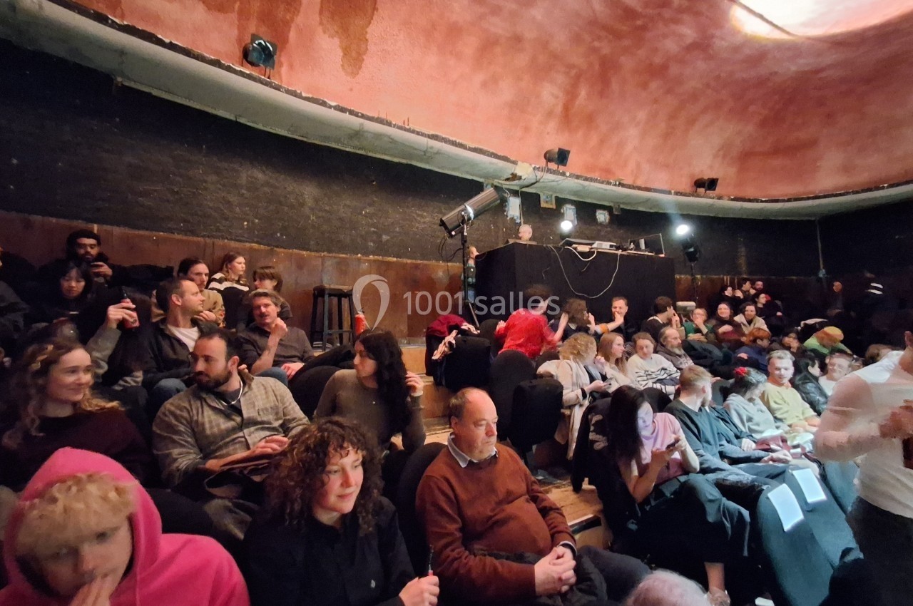 Personnes assises dans une salle de spectacle à l'ambiance tamisée, avec un plafond voûté rougeâtre.