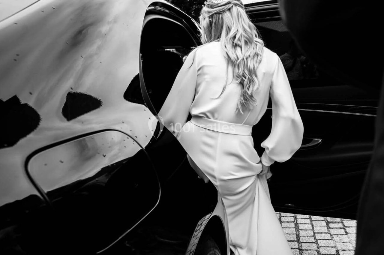 Une femme en robe élégante entre dans une voiture noire, capturée en noir et blanc.