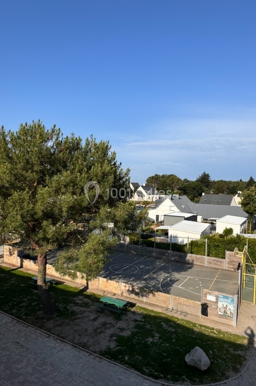 Terrain de basket en plein air entouré d'arbres et de maisons sous un ciel dégagé.