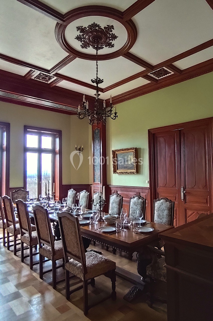 Salle à manger élégante avec une grande table en bois, des chaises assorties et un lustre suspendu au plafond décoré.