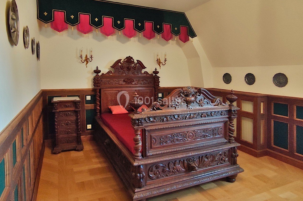 Lit en bois sculpté dans une chambre décorée de panneaux muraux, tentures et appliques murales anciennes.