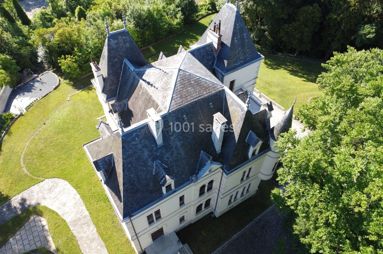 Vue aérienne d'un château à l'architecture classique entouré de jardins et d'arbres verdoyants.