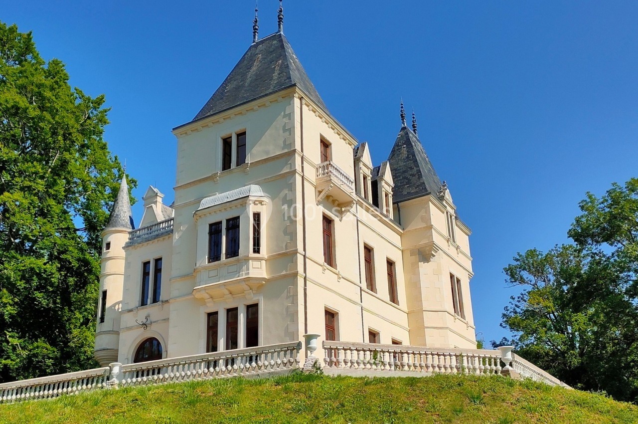 Château blanc à quatre tours, entouré de verdure, sous un ciel bleu dégagé.