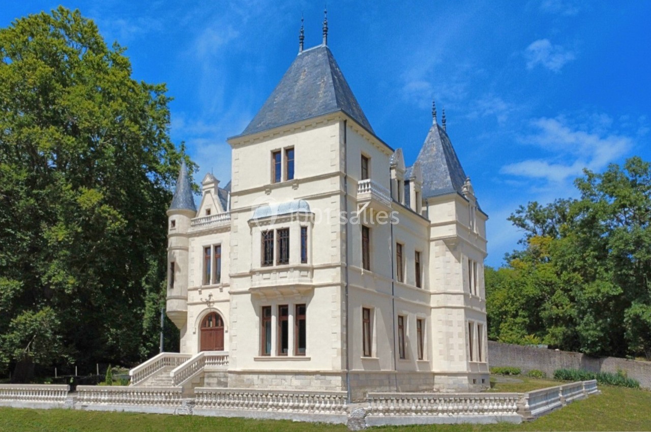 Château blanc à plusieurs tours, entouré d'arbres, sous un ciel bleu clair.