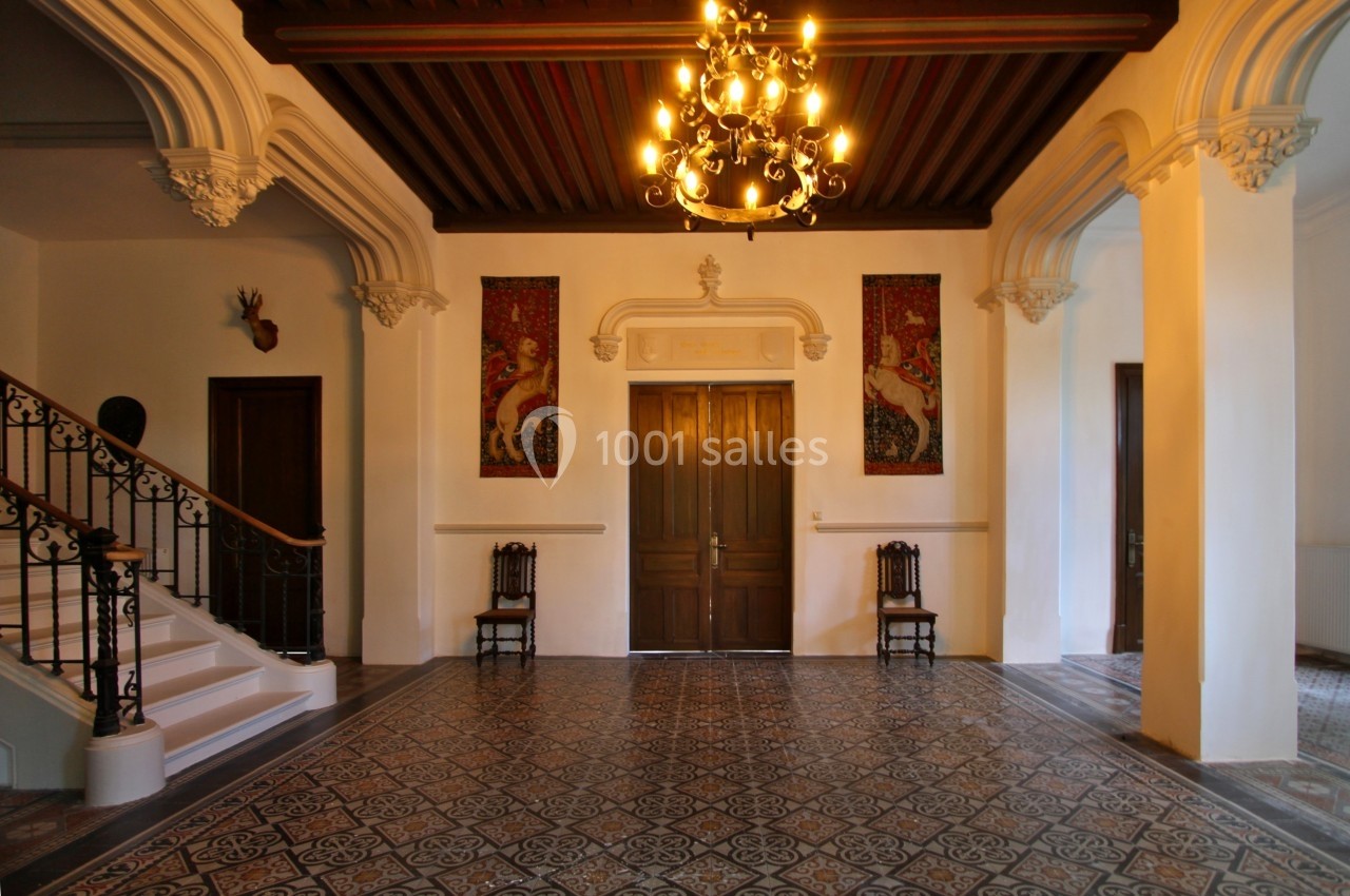 Hall spacieux avec carrelage décoratif, escalier en fer forgé, lustre suspendu et tapisseries murales.