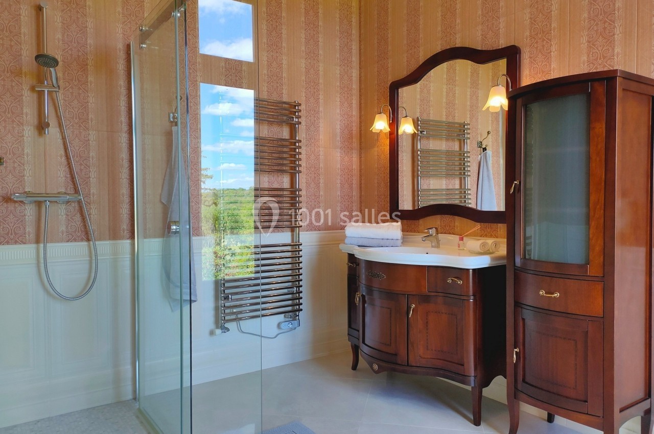 Salle de bain avec douche vitrée, meuble en bois avec miroir, lavabo, et radiateur sèche-serviettes.