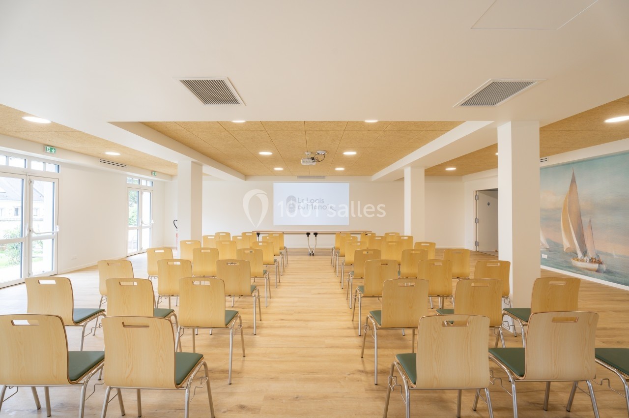 Salle de conférence lumineuse avec des chaises en bois disposées face à un écran de projection.