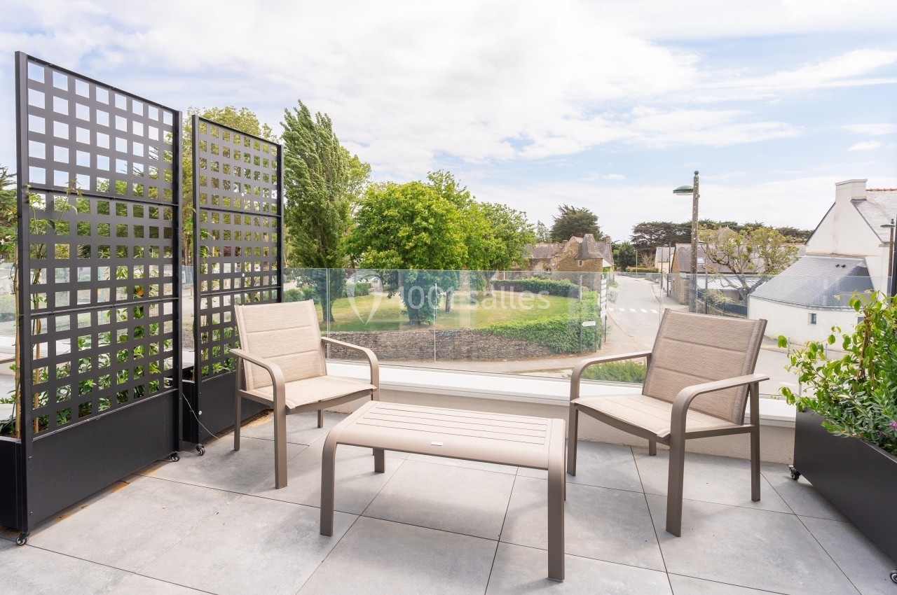 Terrasse avec deux chaises, une table basse, des panneaux décoratifs et vue sur un jardin et des maisons.