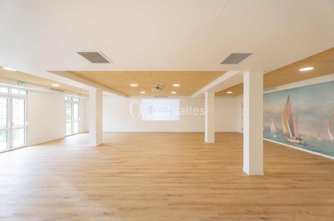 Salle lumineuse avec parquet clair, murs blancs, plafond en bois, et fresque murale représentant des voiliers.