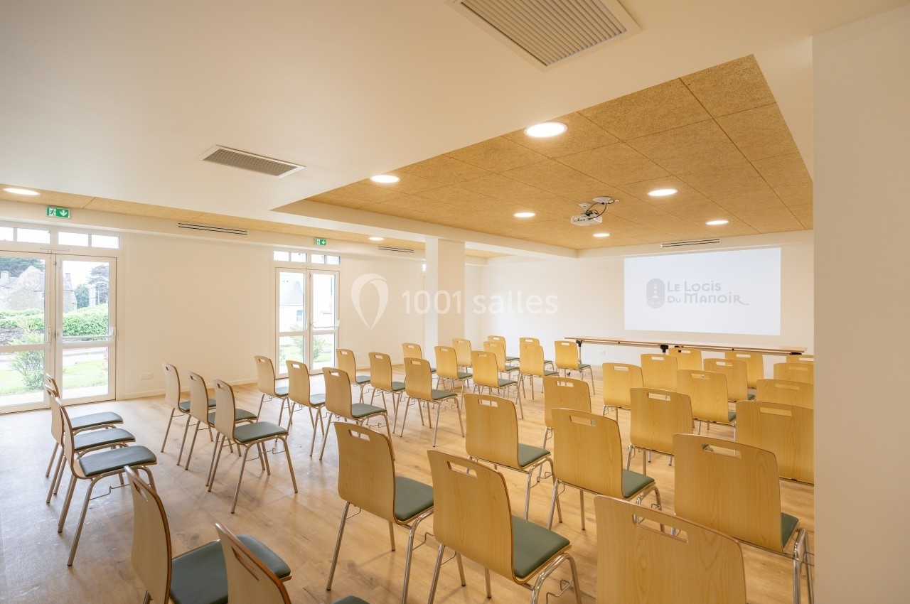 Salle de conférence lumineuse avec chaises disposées en rangées face à un écran de projection.