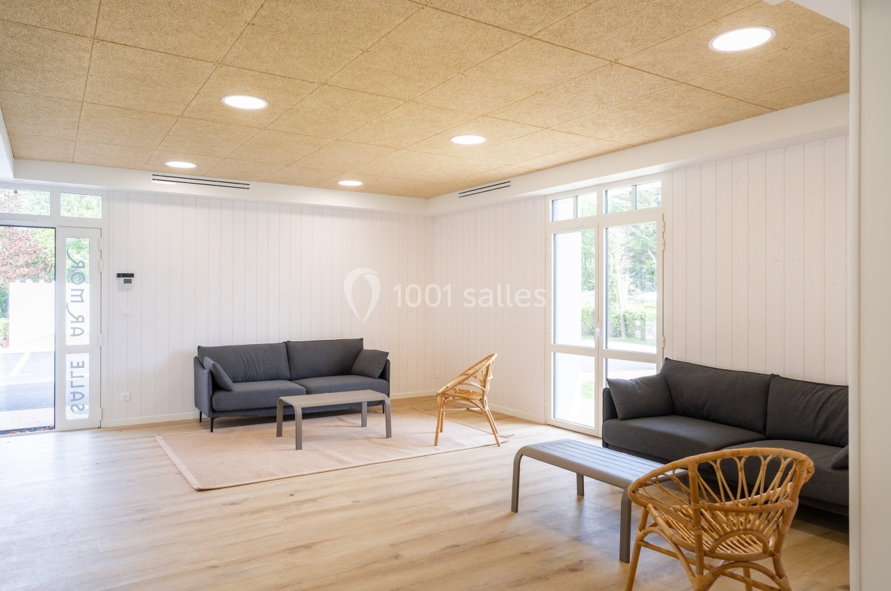 Salle d'attente lumineuse avec canapés gris, fauteuils en rotin, parquet clair et plafond en panneaux de bois.
