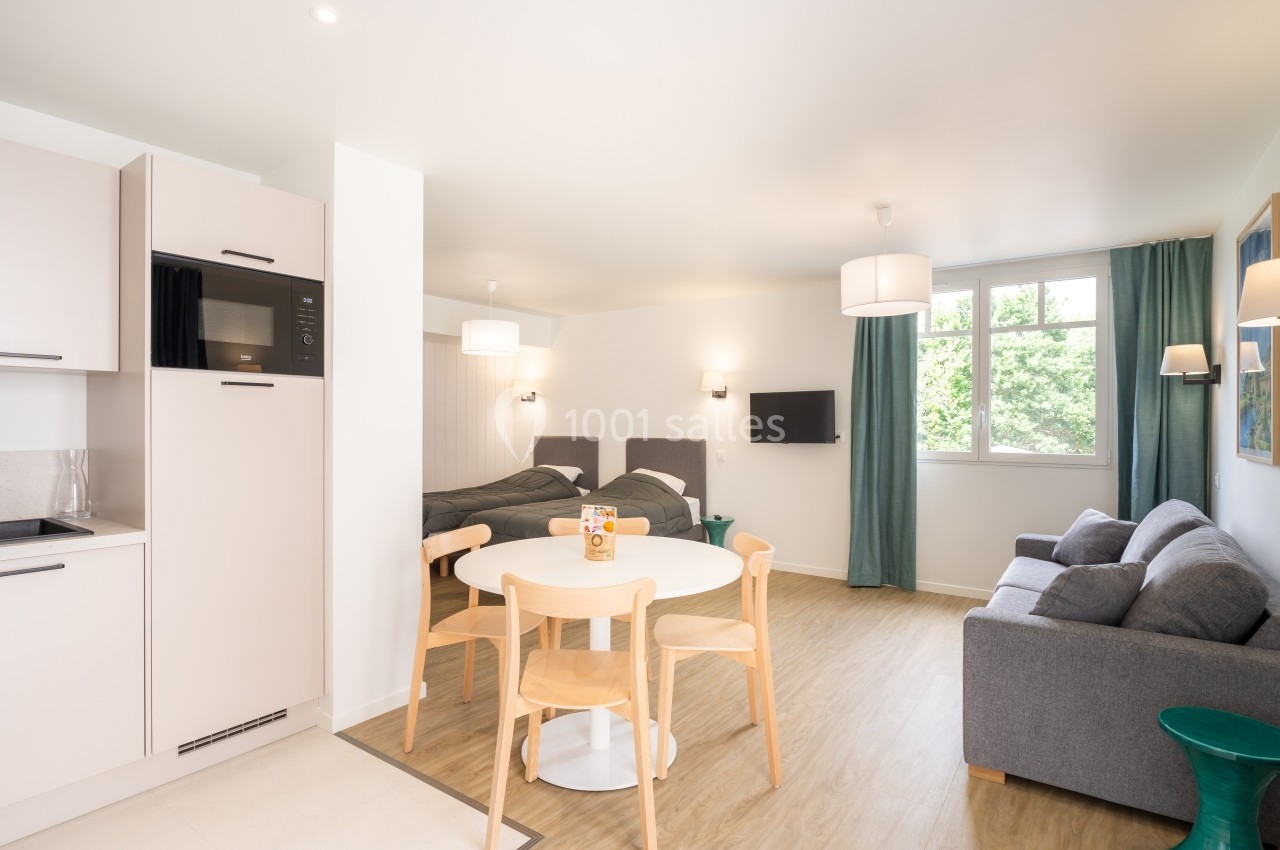 Studio lumineux avec kitchenette équipée, table à manger, canapé, deux lits simples et grande fenêtre donnant sur l…