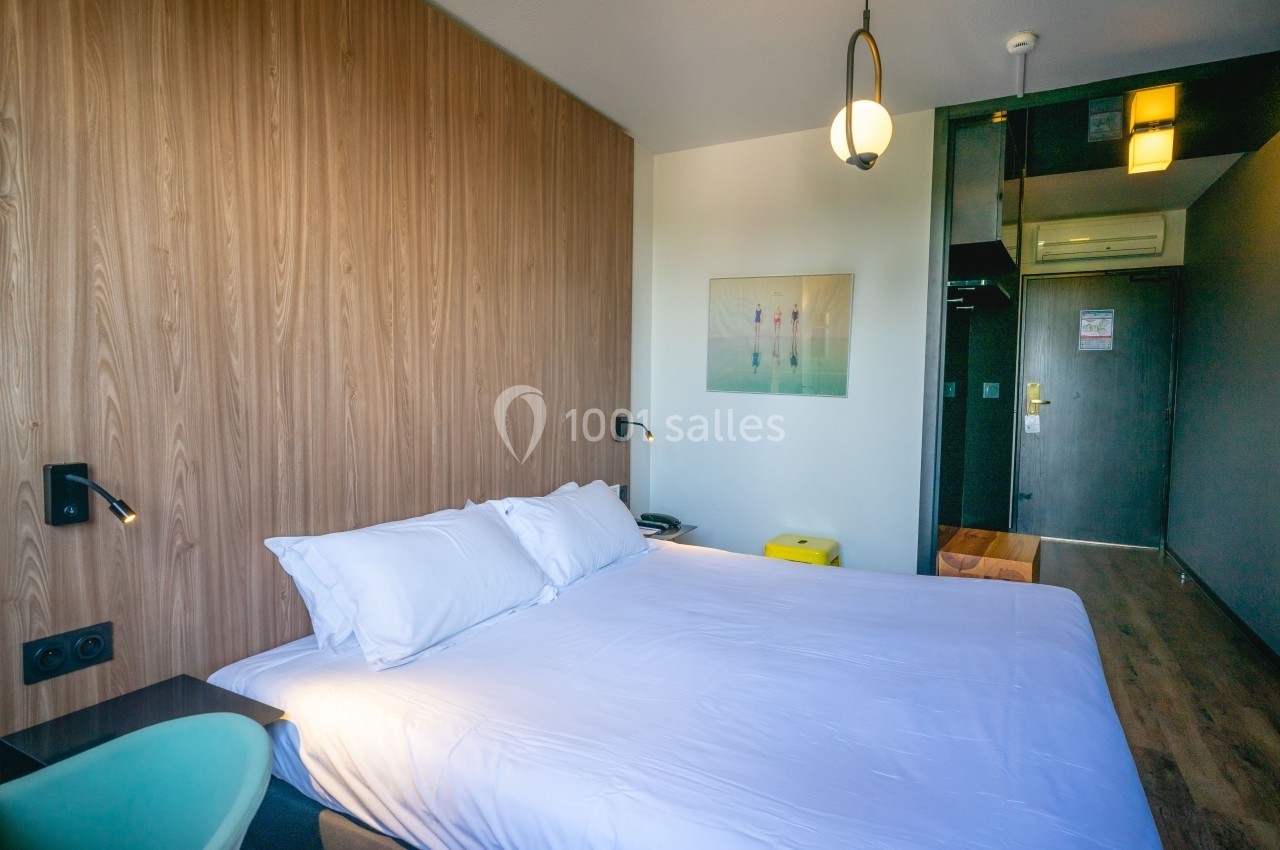 Chambre d'hôtel moderne avec lit double, mur en bois, éclairage suspendu et mobilier minimaliste.