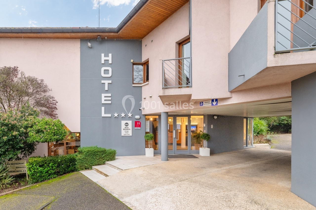 Façade d'un hôtel moderne avec entrée principale, signalétique et végétation environnante.