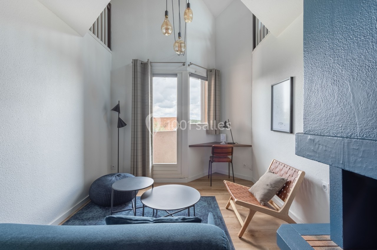 Petit salon lumineux avec canapé, table basse, chaise en bois, bureau près d'une fenêtre et suspension moderne.
