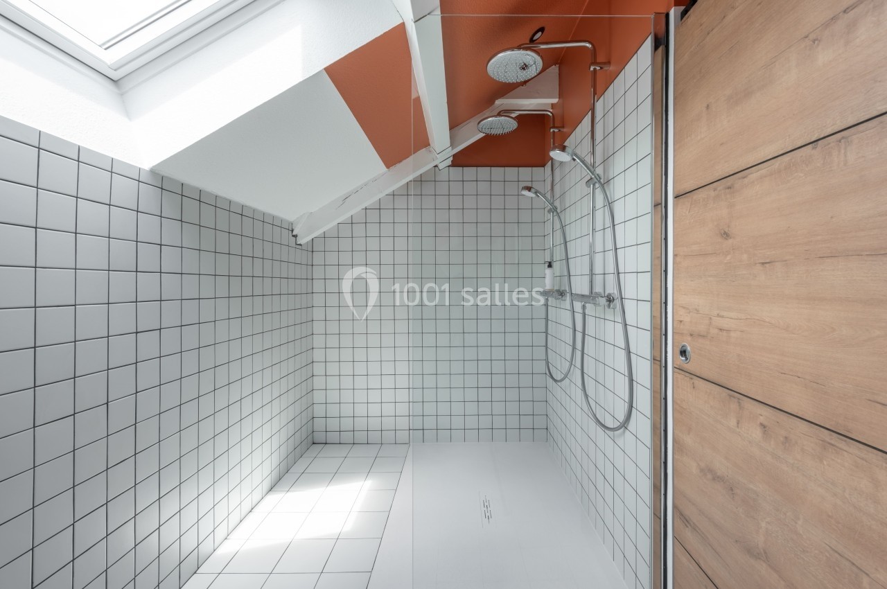 Douche moderne avec carrelage blanc, double pommeau et plafond incliné sous une lucarne.
