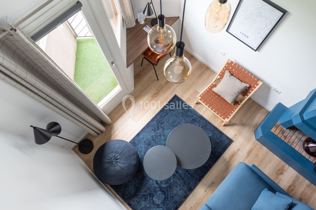 Vue aérienne d'un salon moderne avec canapé bleu, tapis bleu, tables basses rondes et bureau près d'une fenêtre.