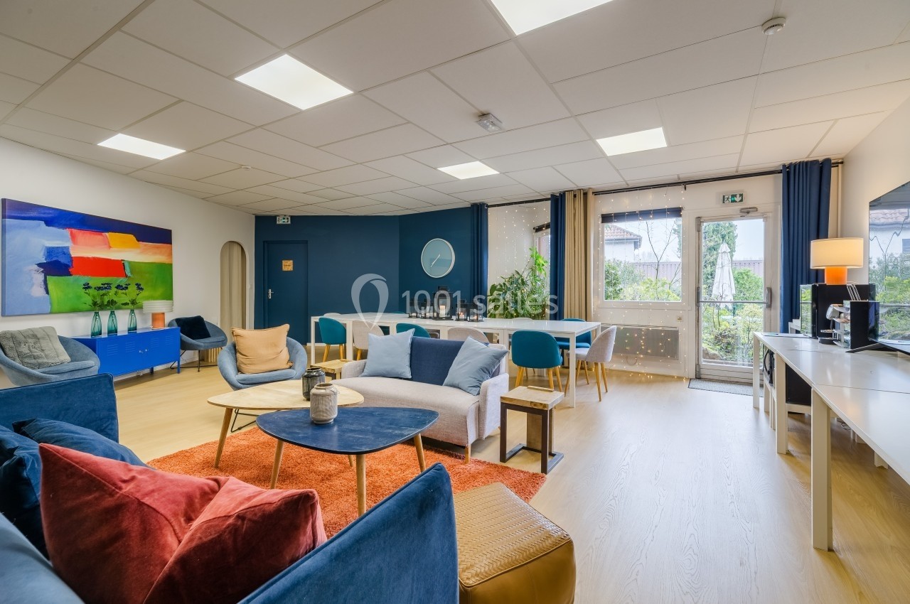 Salle lumineuse avec canapés colorés, table basse, décoration moderne et grandes fenêtres donnant sur un jardin.