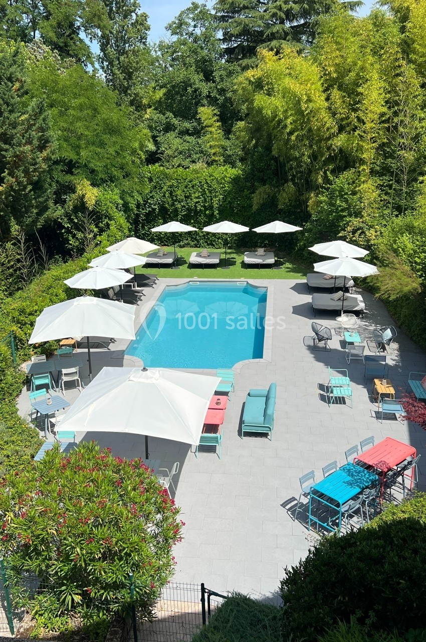 Piscine extérieure entourée de transats, parasols blancs et végétation dense dans un cadre ensoleillé.