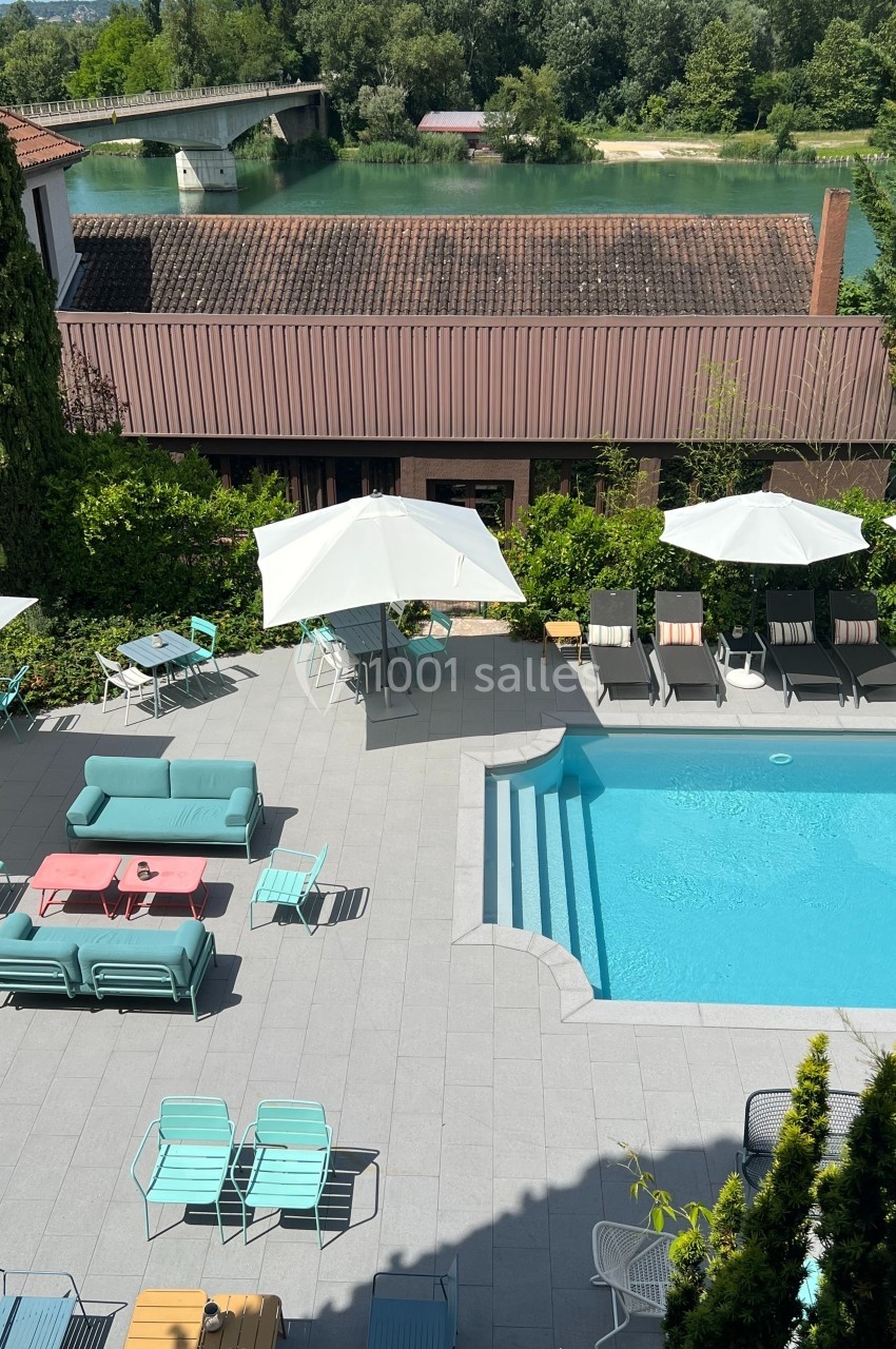 Vue d'une terrasse avec piscine, chaises longues, parasols et rivière en arrière-plan.