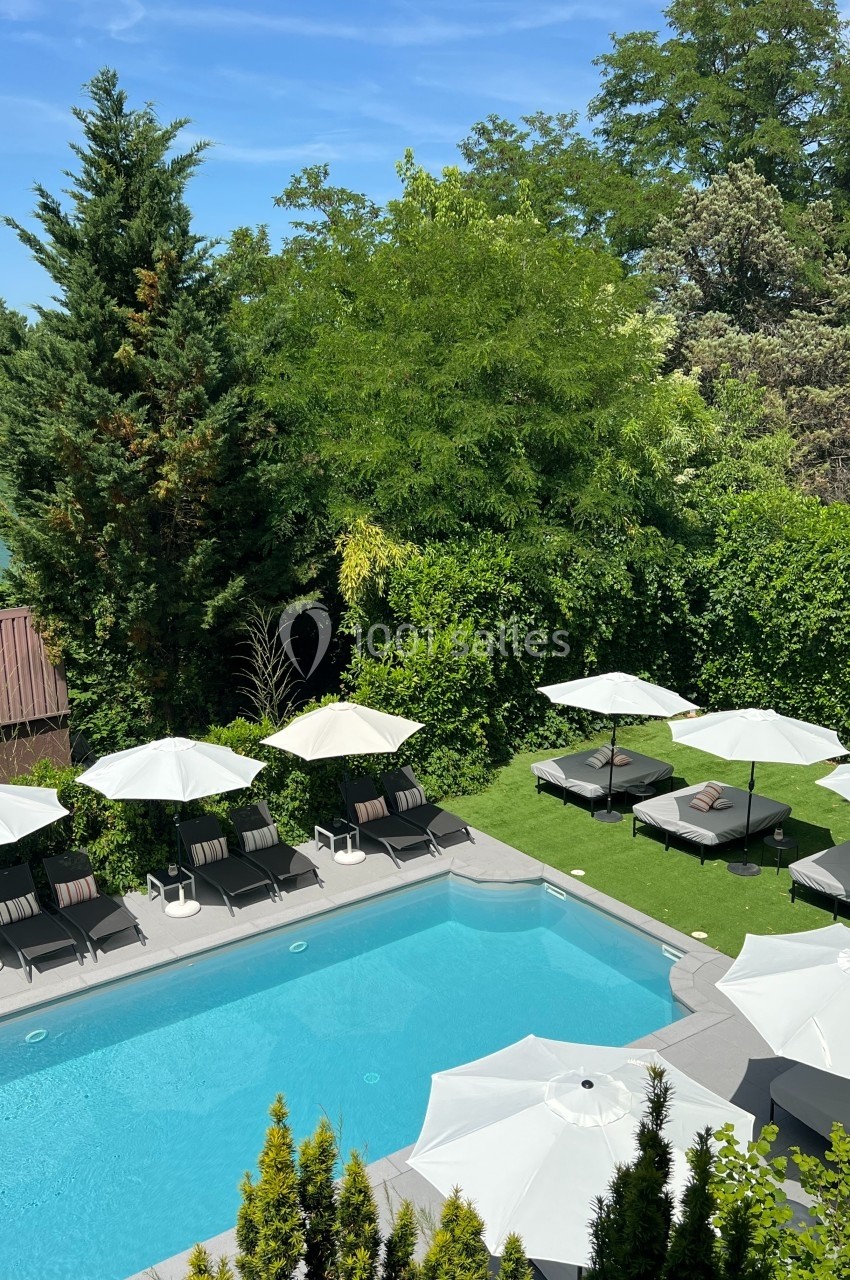 Piscine extérieure entourée de transats avec parasols blancs, bordée de pelouse et d'arbres verdoyants.