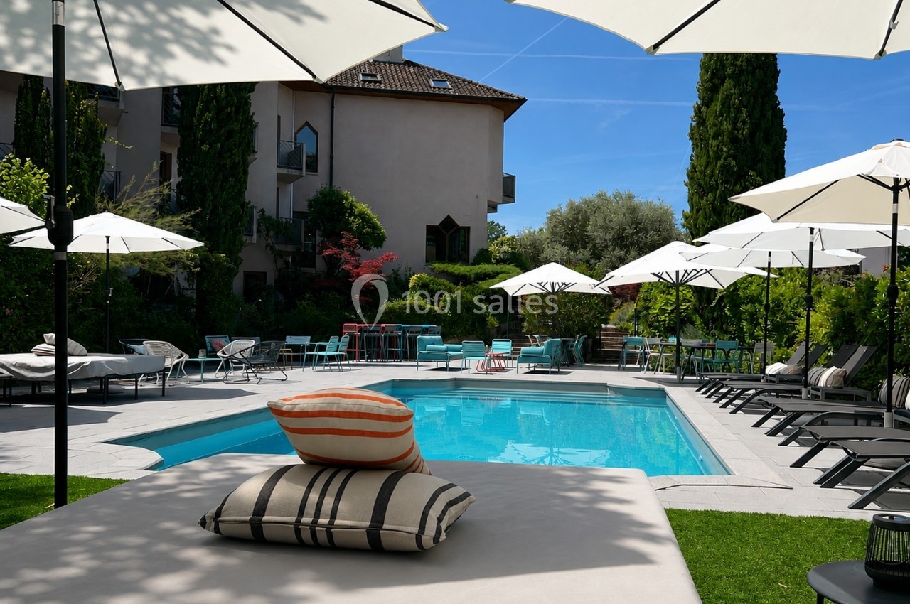 Piscine extérieure entourée de transats, parasols blancs et végétation luxuriante par une journée ensoleillée.