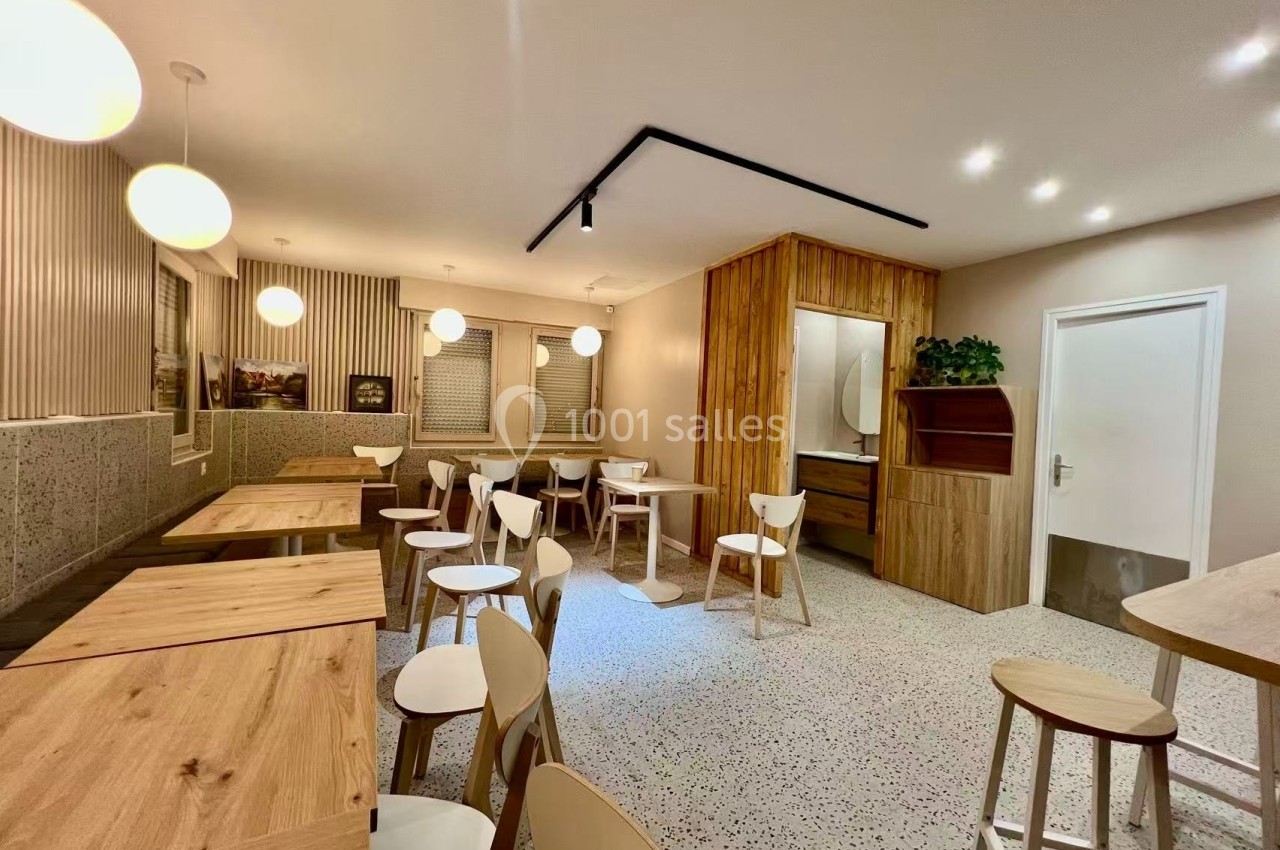 Salle de restaurant moderne avec tables en bois clair, chaises blanches et éclairage suspendu dans un décor épuré.
