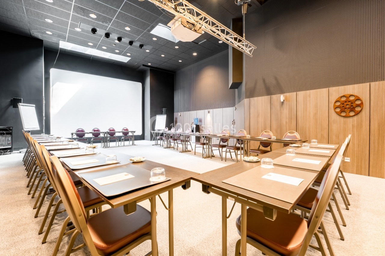 Salle de réunion lumineuse avec tables disposées en U, chaises alignées et matériel de présentation.