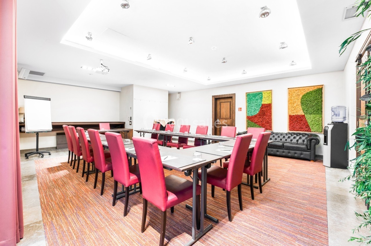 Salle de réunion lumineuse avec des chaises rouges, une grande table, un tableau de conférence et des décorations murales…