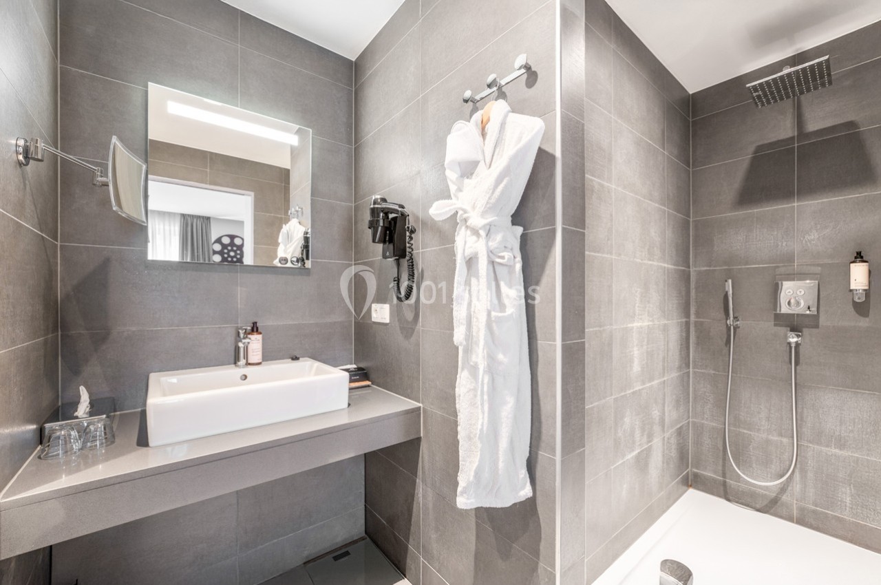 Salle de bain moderne avec douche à l'italienne, lavabo, miroir, sèche-cheveux et peignoir suspendu.
