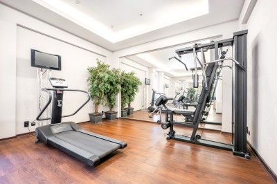 Salle de sport lumineuse avec vélos d'exercice, tapis de course et miroir mural, sol en bois.