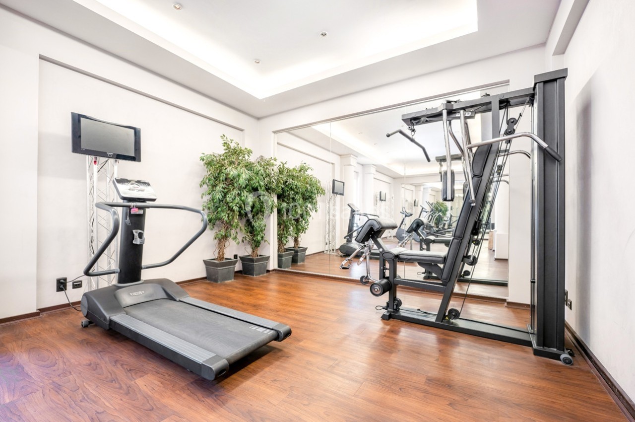 Salle de sport avec tapis de course, machine de musculation, miroir mural et plantes décoratives.