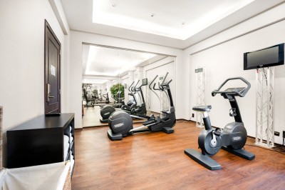Salle de sport lumineuse avec vélos d'exercice, tapis de course et miroir mural, sol en bois.