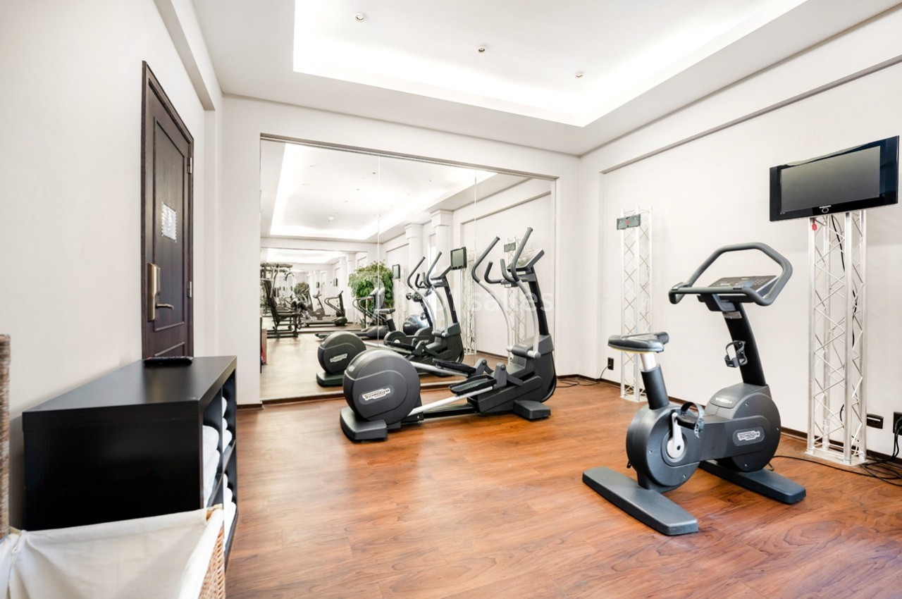 Salle de sport lumineuse avec vélos d'exercice, tapis de course et miroir mural, sol en bois.
