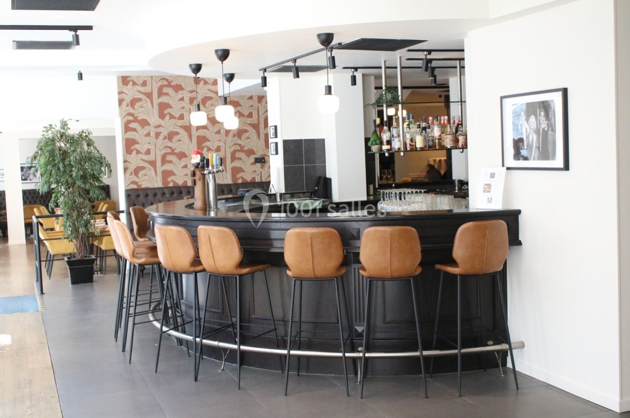 Bar arrondi avec tabourets en cuir, décor moderne, plantes et étagères garnies de bouteilles à l'arrière-plan.