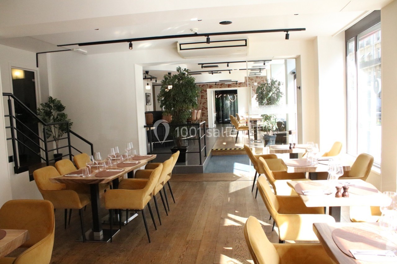 Salle de restaurant lumineuse avec des tables dressées, des chaises jaunes et des plantes décoratives.