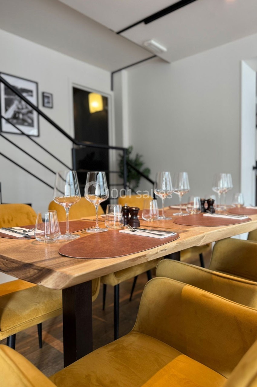 Salle de restaurant moderne avec tables en bois, chaises jaunes, verres et couverts disposés pour un repas.