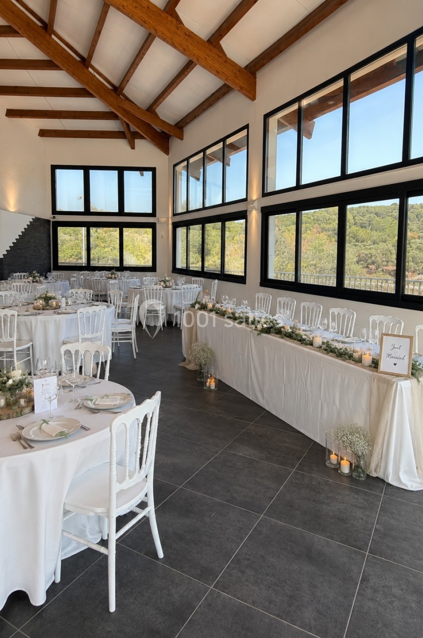 Salle de réception lumineuse avec tables décorées pour un événement, grandes baies vitrées et vue sur la nature.