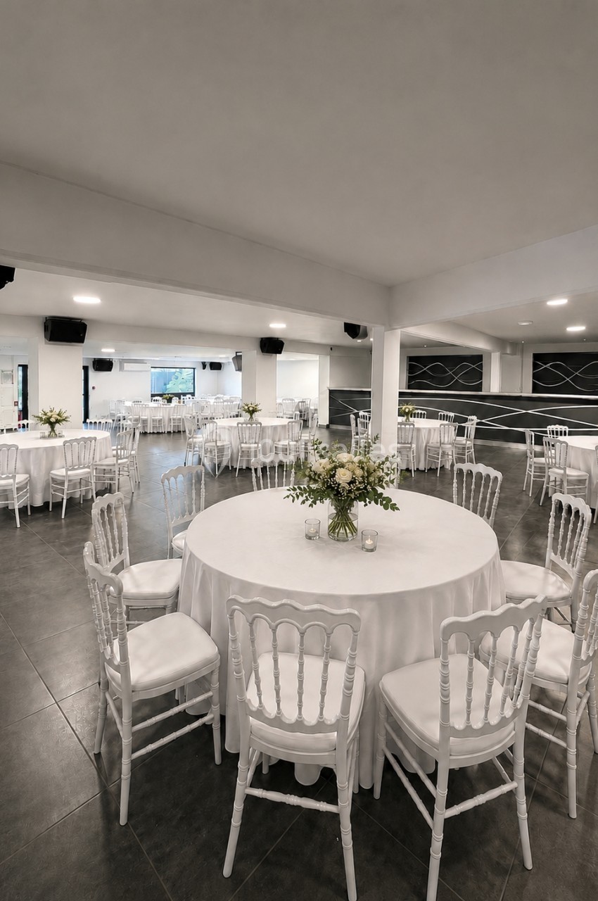 Salle de réception élégante avec tables rondes dressées, nappes blanches et chaises assorties, décor floral central.