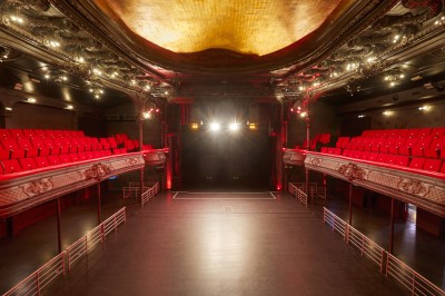 Intérieur d'une salle de spectacle avec balustrade, colonnes décoratives et éclairage tamisé.