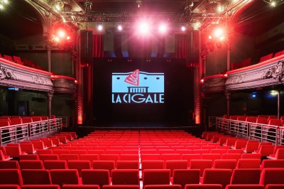 Hall d'entrée avec murs aux formes ondulées, sol à motifs géométriques et escalier menant à une porte noire.