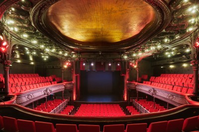Hall d'entrée avec murs aux formes ondulées, sol à motifs géométriques et escalier menant à une porte noire.